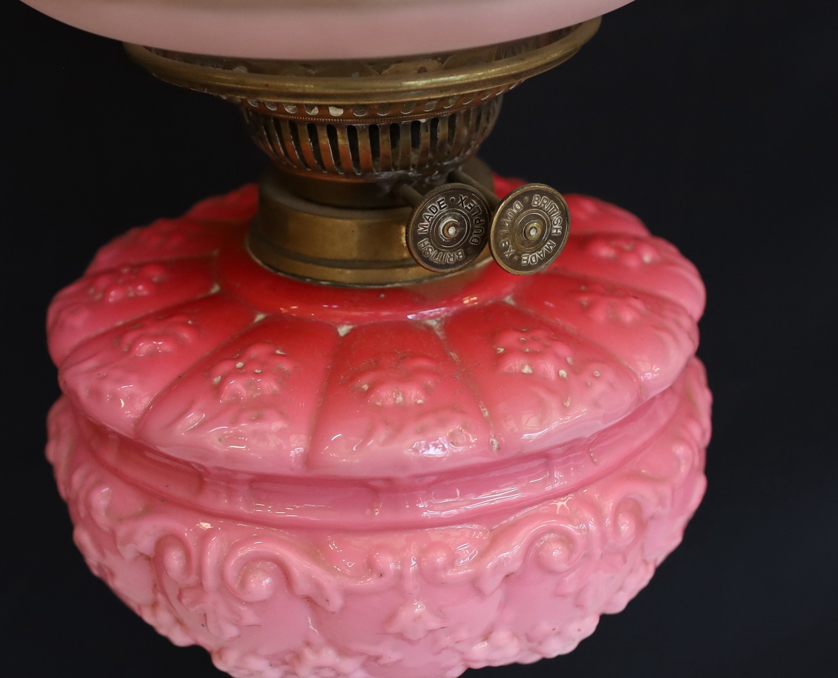 A late Victorian brass oil lamp with opaque pink glass reservoir, duplex mechanism, cranberry tinted etched glass shade and flue, height overall 65cm